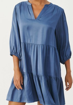 Niebieska sukienka o luźnym kroju z trój-ćwierć rękawami i warstwową spódnicą, widok na sylwetkę od pasa wzwyż.