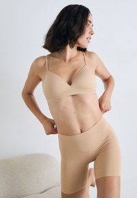 Beige naadloze bh met dunne bandjes en een V-hals ontwerp, gecombineerd met hoogsluitende, strakke beige shorts die een soepele textuur benadrukken.