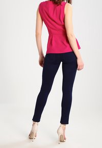 Top peplum senza maniche fucsia abbinato a jeans skinny blu scuro e sandali con tacco beige, visto da dietro.