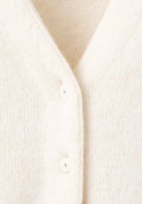 Cárdigan de crema claro hecho de tela suave y texturizada con escote en V y dos botones blancos en la parte delantera, con detalles acanalados.