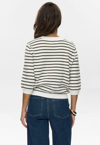 Randig tröja i vitt och brunt med en strukturerad stickning, trekvartslånga ärmar och en ribbad nederkant. Kombinerad med mörkblå jeans.