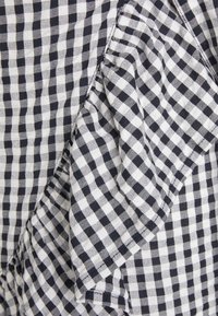 Tela de cuadros en blanco y negro con un detalle de volante, presenta un patrón a cuadros. El material parece liviano y texturizado.