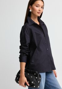 Sort skjorte med spredekrave og subtile prikmønstre. Sammen med en sort læderclutch med metalliske nitter og afrundet design.