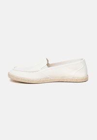 Scarpe bianche senza lacci con tomaia in tela testurizzata, dettagli laterali elasticizzati e suola in corda di juta. Design a profilo basso con cuciture minime.