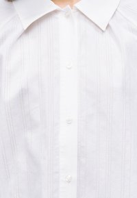 Λευκό πουκάμισο με κουμπιά και διακριτικό κάθετο ριγέ σχέδιο, με μυτερό γιακά.