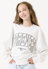 Sudadera gris claro de corte oversize. Presenta "FOREVER" en una fuente negra en negrita y texto más pequeño debajo. Tejido suave y puños acanalados.