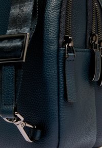 Borsa in pelle blu scuro con superficie strutturata, presenta molteplici cerniere, tracolla regolabile e dettagli in metallo argentato.