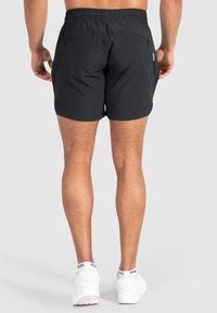 Pantalones cortos negros de material ligero, con una cinturilla elástica y dos bolsillos con cremallera en la parte trasera. Diseñados para la comodidad.