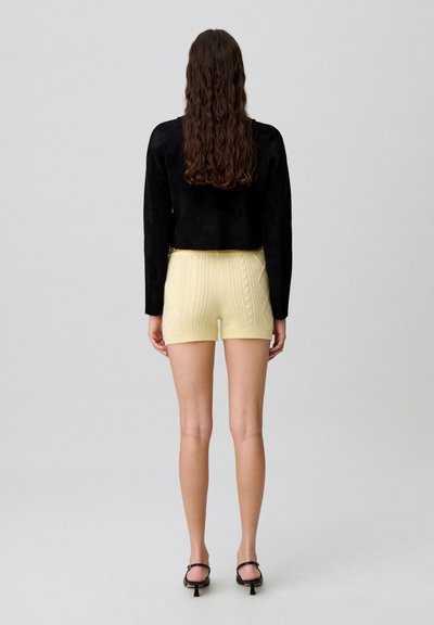 Top corto negro y pantalones cortos de punto amarillos con patrones de textura. Los pantalones cortos tienen una cinturilla acanalada y son de longitud media en el muslo.