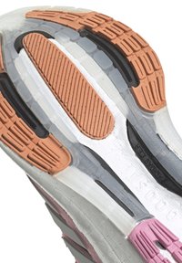 Sula av sko med en blandning av gummi och genomskinliga material, med rosa, orange och svarta accenter, mönstrad nöt och textbranding.