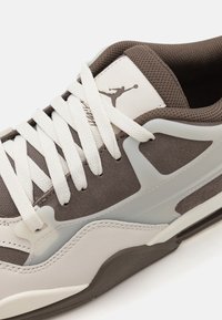 Baskets avec un design blanc et marron, présentant du daim texturé et du cuir lisse. Comprend des lacets blancs et un panneau semi-transparent.