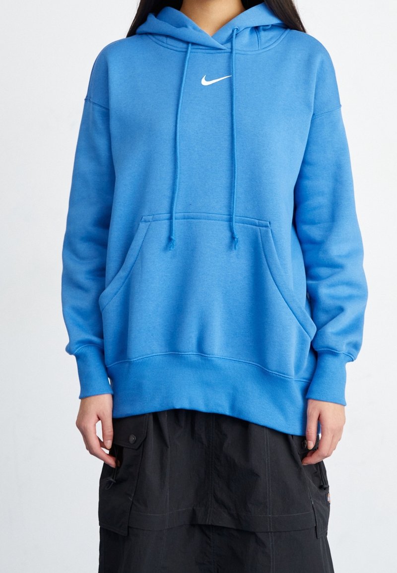 Blå hoodie gjord av mjukt material, med en känguruficka, huva med dragsko och vit Nike-logotyp. Ribbstickade muddar och fåll.