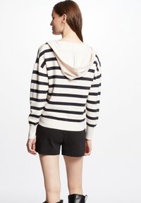 Gestreepte hoodie in crème en marineblauw, met een textuurstof, grote capuchon en geribbelde mouwen. Draag het met zwarte shorts en kniehoge laarzen.