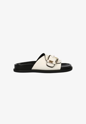 Zwart-witte schuifslipper met een brede band en een grote gouden gesp op een platte zool.