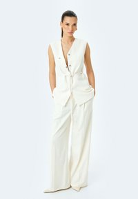 Weißer ärmelloser Jumpsuit mit V-Ausschnitt, Knopfverschluss vorne, seitlichen Taschen und Taillengürtel, mit einem maßgeschneiderten, weiten Bein-Design.
