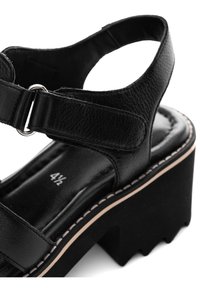 Sandale compensée en cuir noir avec bride à la cheville, fermeture réglable à scratch et taille 4,5 indiquée sur la semelle rembourrée.