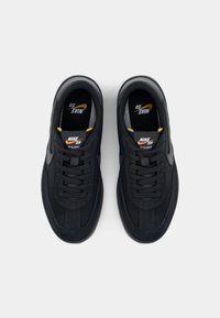 Chaussures Nike SB noires en daim et matériaux synthétiques, avec des lacets plats, un col rembourré et des accents jaunes sur le logo de la languette.