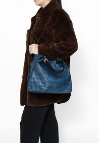 Borsa a tracolla in pelle tessuta blu con una forma strutturata e una tracolla nera. La borsa ha una superficie testurizzata e cuciture a contrasto.