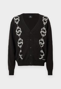 Cardigan noir à boutons avec des motifs de serpent et de dés blancs courant verticalement des deux côtés de l'avant.