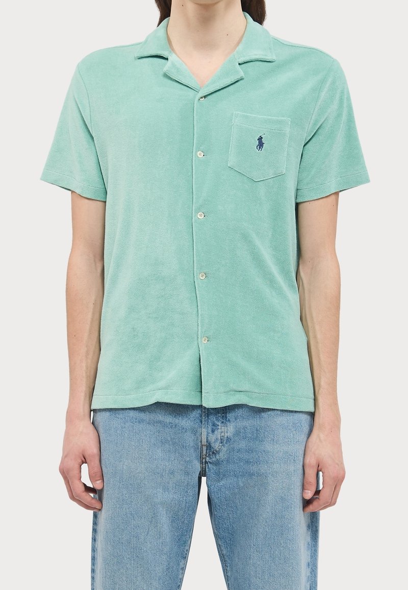 Camicia a maniche corte verde chiaro in morbido terrycloth, con abbottonatura frontale, una tasca sul petto e un piccolo logo.