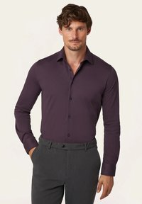 Dunkellila Langarmshirt mit kragenförmigem Ausschnitt, Knopfleiste vorne und schwarzen Knöpfen; aus einem glatten, leichten Stoff gefertigt.