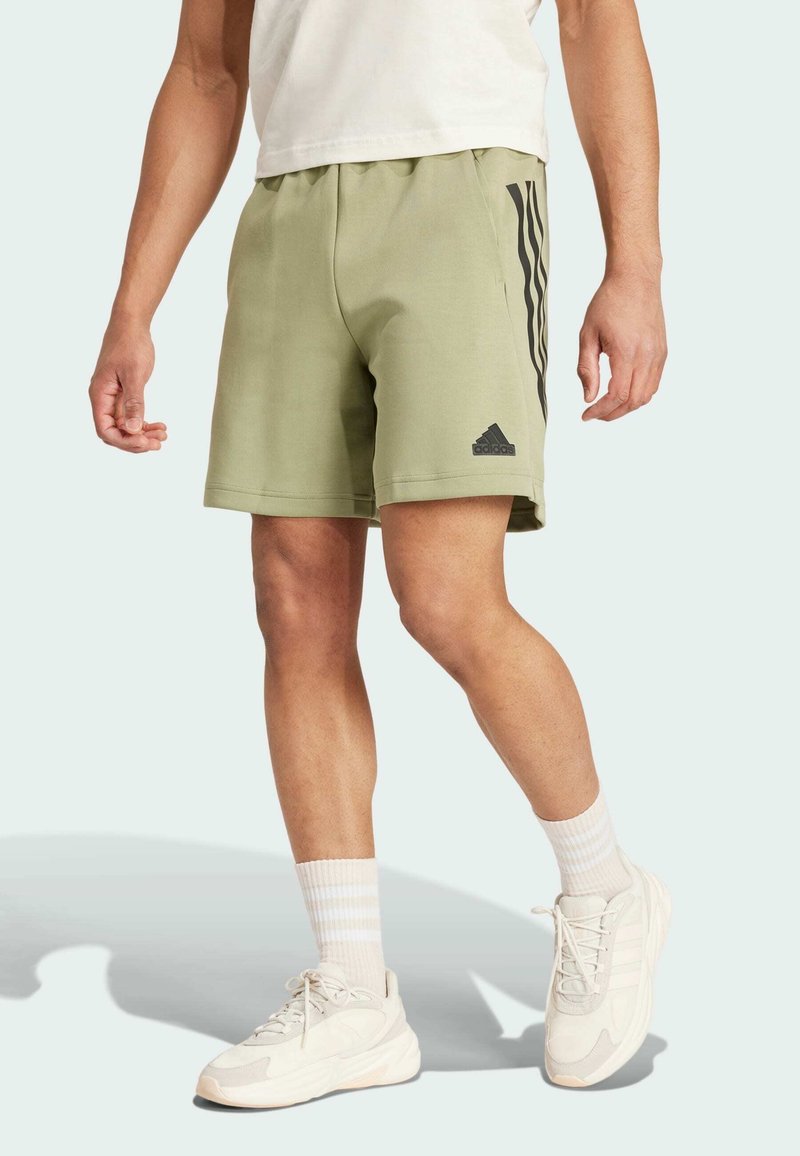Zelené sportovní šortky s elastickým pasem, s třemi černými pruhy po stranách a logem Adidas na lemu.