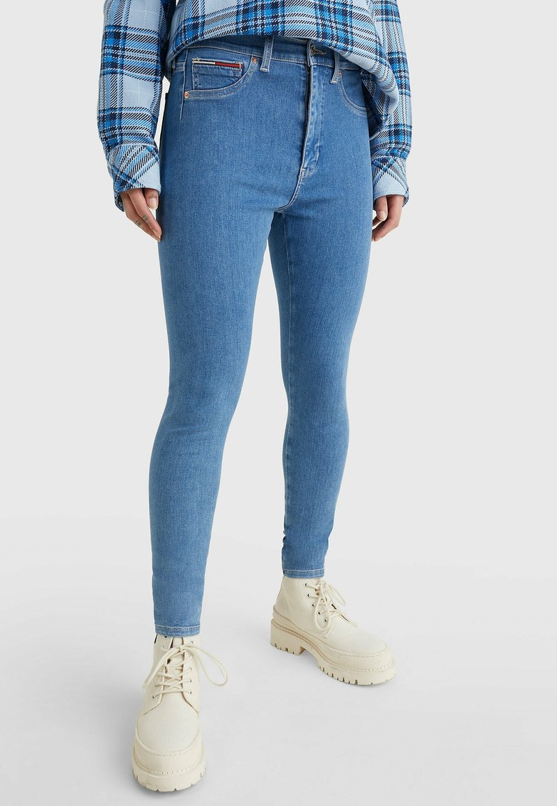 Jeans skinny de mezclilla azul claro con cintura alta, costura detallada y un bolsillo frontal, combinados con botas gruesas de color crema.