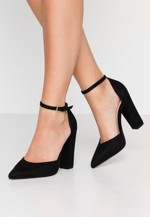 Czarne zamszowe szpilki z wąskim noskiem i grubym klockowym obcasem, z delikatnym paskiem na kostce zapinanym na złotą klamrę.