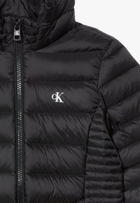 Black puffer jacket with a quilted design and a zip closure. Features a small white logo on the left side, soft texture, and hood.