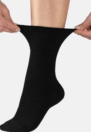 Black cotton sock being stretched, featuring a ribbed top and smooth texture. The foot is partially visible, emphasizing the sock's fit.