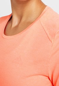 Licht koraalkleurig T-shirt met korte mouwen, voorzien van een ronde halslijn en een textuurstof met een subtiel patroon. Duidelijke naaddetails op de schouders.