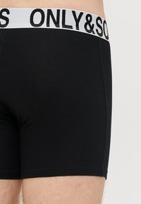 Czarne bokserki bawełniane z białą elastyczną gumą w pasie, na której znajduje się nazwa marki "ONLY & SONS" w czarnych literach.