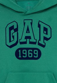 Hoodie vert GAP Kids avec un grand texte navy "GAP 1969" sur la poitrine et une poche frontale visible.