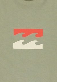 Grafisch T-shirt in olijfgroen stof met een rood en crèmekleurig golfontwerp in een rechthoekige opstelling in het midden.