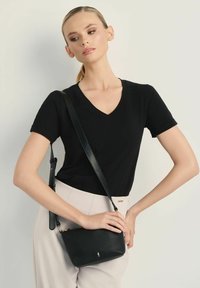 Czarna skórzana torba na ramię z złotym akcentem, prostokątny kształt i regulowany pasek, w zestawieniu z czarnym T-shirtem z dekoltem w serek i jasnymi spodniami.