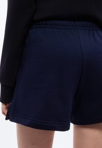 Κοντινό πλάνο ατόμου που φοράει σορτς με ελαστική μέση σε ναυτικό μπλε χρώμα και μαύρο μακρυμάνικο τοπ, που δείχνει το κάτω μέρος της πλάτης και το άνω μέρος των μηρών.