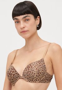 Leopard print bra with smooth beige fabric, seamless cups, and adjustable tan straps, highlighting a subtle animal pattern and soft texture.