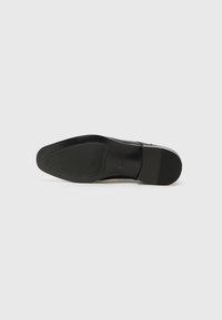 Suela de zapato de cuero negro con un acabado suave, forma redondeada, patrón de agarre texturizado y un ligero tacón. Sin marcas visibles ni adornos.