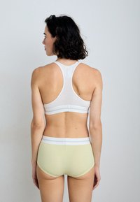White ribbed sports bra with a racerback design, paired with light green ribbed high-waisted shorts featuring white elastic waistband.