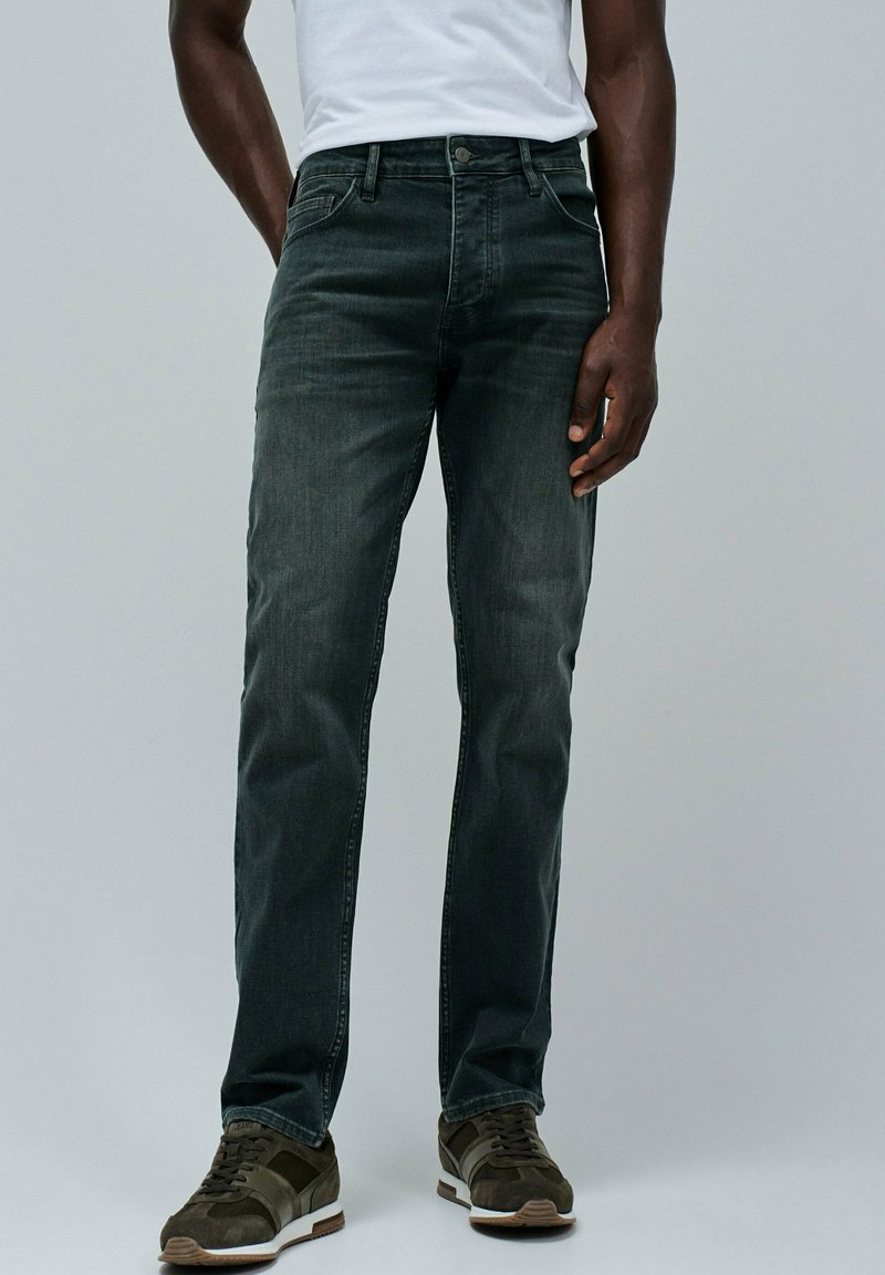 Jeans in denim grigio scuro con design a gamba dritta, dotati di cinque tasche, leggera sfumatura e chiusura con bottone in metallo. Abbinati a sneaker scure.