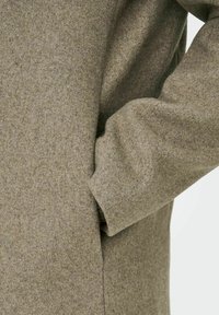 Villane mantel tuhmades oliivrohelises värvitoonis pehme ja tekstuurse viimistlusega. Omab küljetaskut ja lõdva sobivust, millel on madalamad õlavarred.