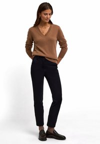 Pullover marrone a scollo a V abbinato a pantaloni neri su misura. Il pullover presenta una texture morbida; i pantaloni sono aderenti con una finitura liscia.
