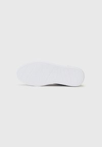 Hvit sneaker-såle med en teksturert gummioverflate som har spor og mønstre for grep. Enkelt design, ingen synlige logoer eller detaljer.