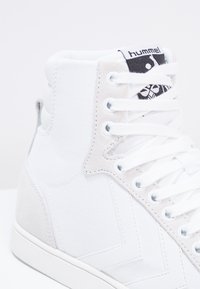 Sneakers de cano alto em lona branca com detalhes em camurça, apresentando um acabamento texturizado, atacadores brancos planos e uma etiqueta com o logótipo na língua.