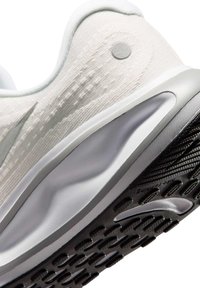 Close-up of a white athletic shoe heel with textured fabric, a silver midsole, and a black rubber outsole with tread patterns.