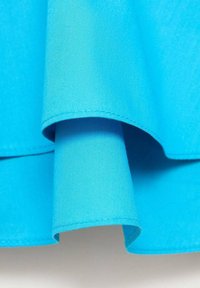 Živá tyrkysová látka s hladkým povrchem, s přeloženými okraji a precizním stehem, která představuje čistý, jednoduše elegantní design.