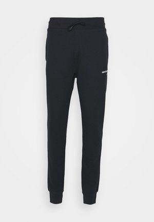 Schwarze, schmal zulaufende Jogginghose mit elastischen Bündchen am Knöchel, einem Kordelzug in der Taille, Seitentaschen und einem kleinen weißen Logo am oberen Oberschenkel.