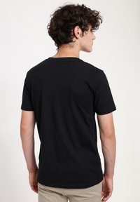 Sort bomulds T-shirt med korte ærmer, rund halsudskæring og et enkelt design. Bagfra ses en glat tekstur uden synlige logoer eller grafik.