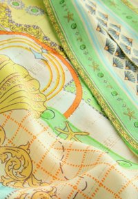 Tessuto multicolore con motivi intricati in giallo, verde e arancione. Presenta conchiglie, stelle e un design a griglia con una consistenza morbida.
