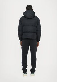 Black puffer jacket with a hood, characterized by a quilted design and spacious silhouette, paired with slim-fitting dark trousers and white shoes.
